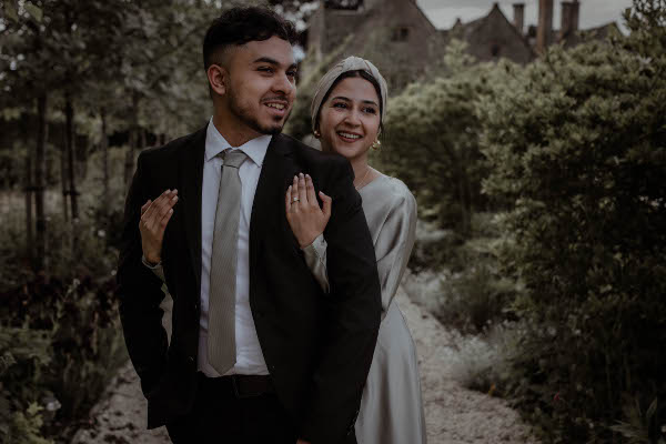 lady in green dress wraps her arms around her fiancé who wears a black suit as the smile into the distance