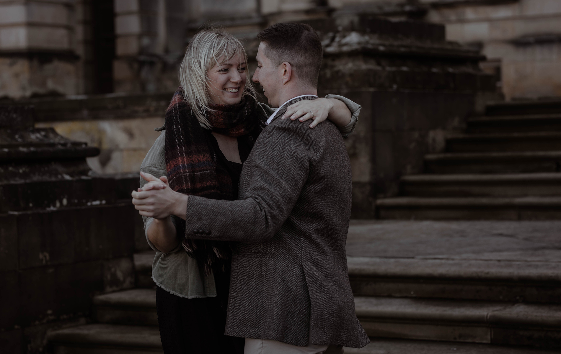 happy engaged couple wearing scarfs and coat slowly dance infront of castle Howard